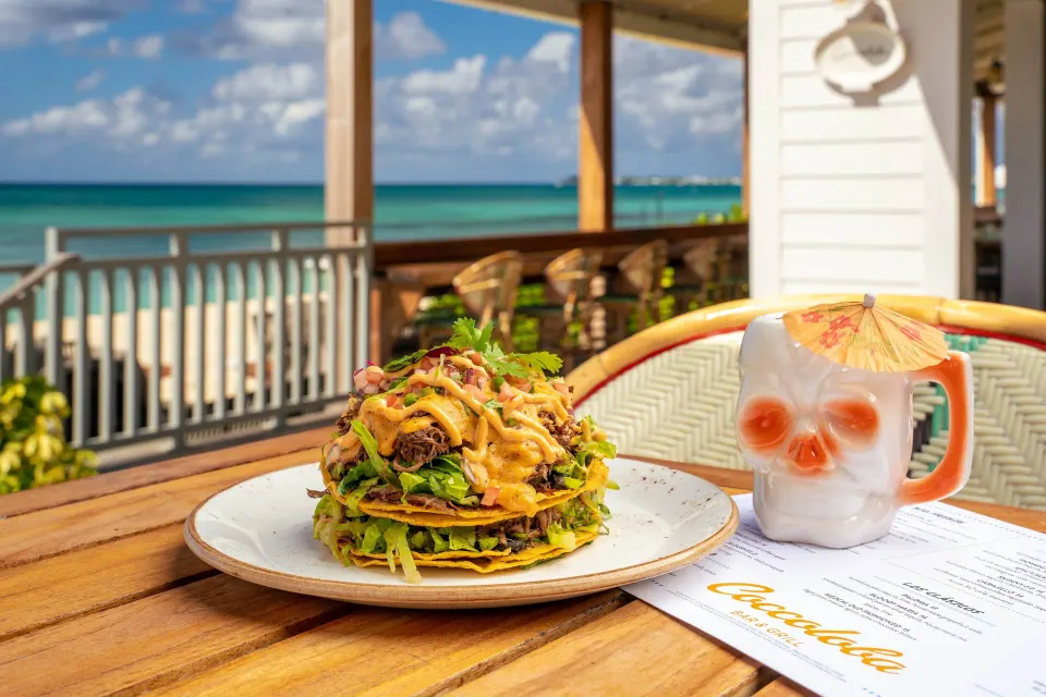 Stacked tacos and a tropical cocktail on a seaside deck with a Coccoloba menu at Kimpton Seafire Resort + Spa.