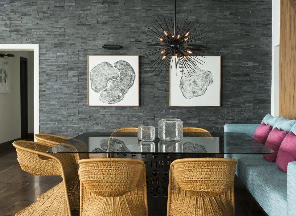 Glass-top dining table with rattan chairs and textured stone wall at Kimpton Seafire Resort + Spa