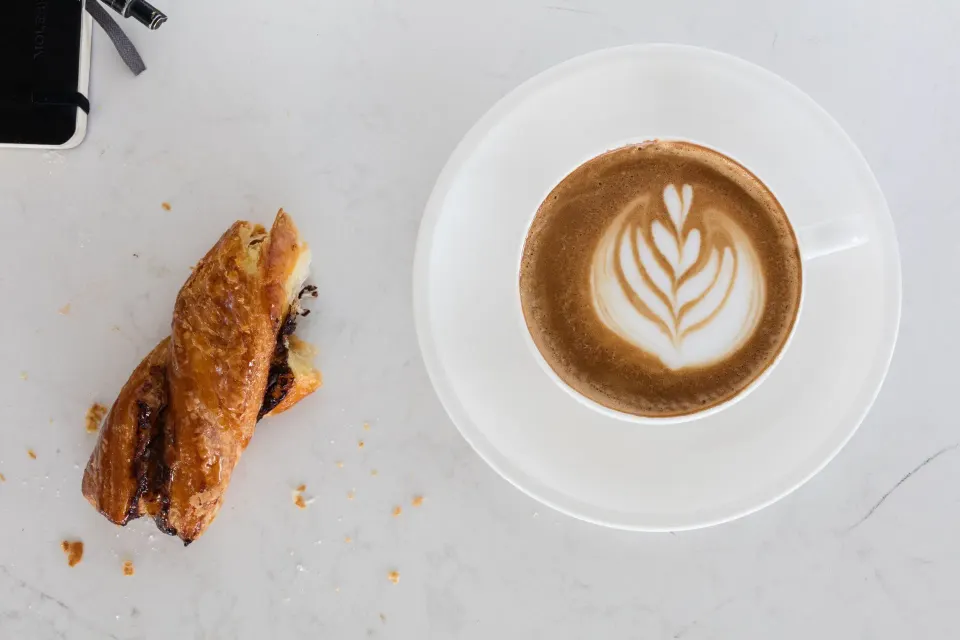 Latte with leaf latte art and a twisted pastry on a marble counter at Kimpton Seafire Resort + Spa