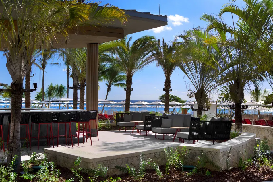 Poolside bar seating and lounge area with palm trees and umbrellas at Kimpton Seafire Resort + Spa