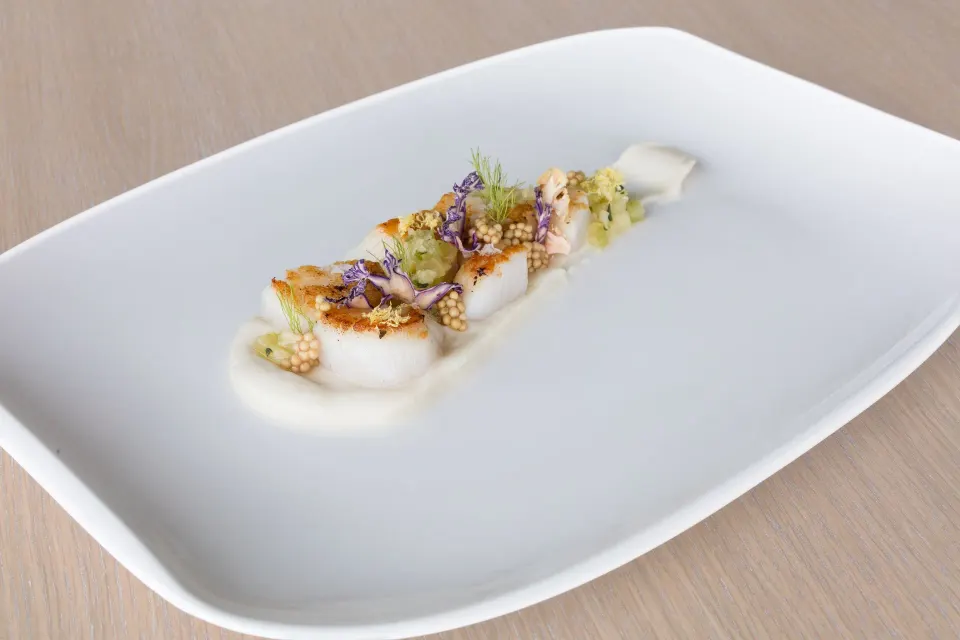 Seared scallops with micro herbs on a white platter at Kimpton Seafire Resort + Spa