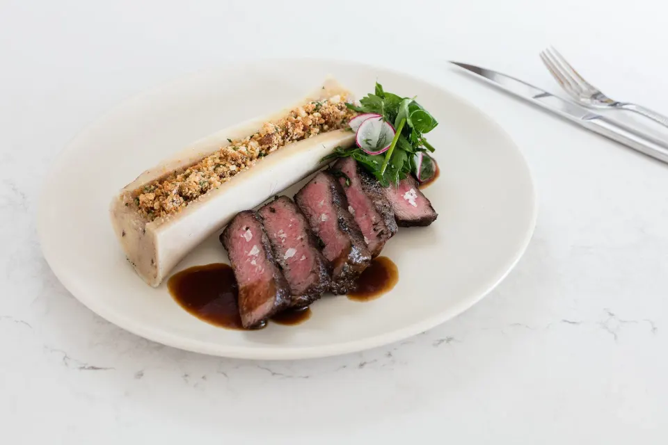 Sliced steak with herb crust and greens on a plate at Kimpton Seafire Resort + Spa