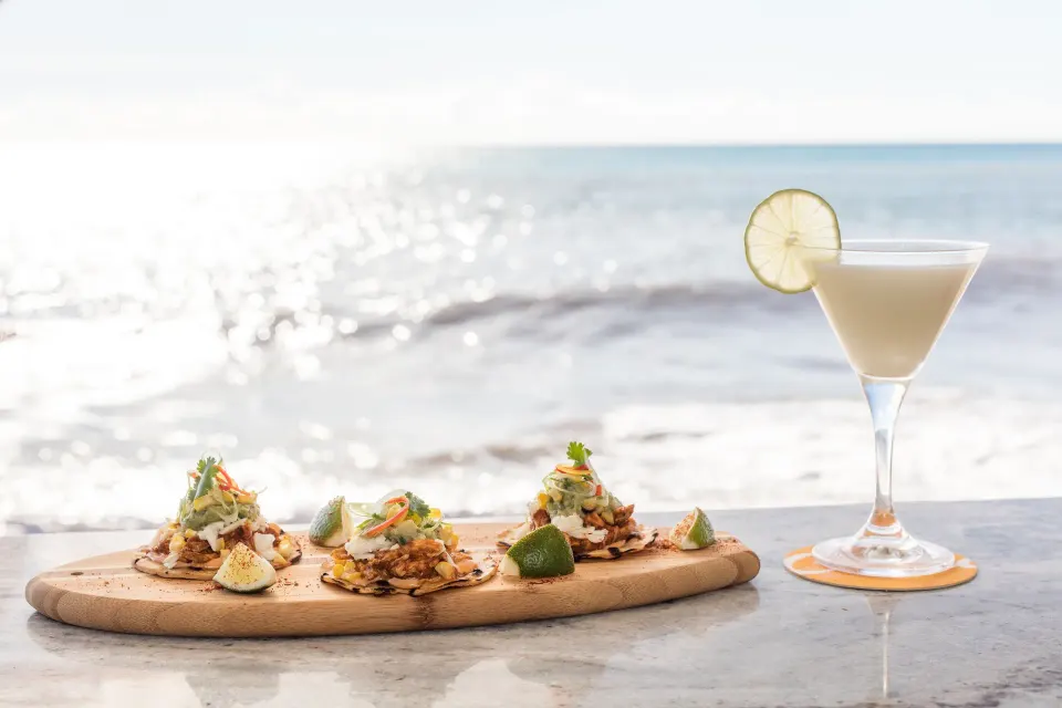 Three small tostadas and a cocktail with the ocean in the background at Kimpton Seafire Resort + Spa
