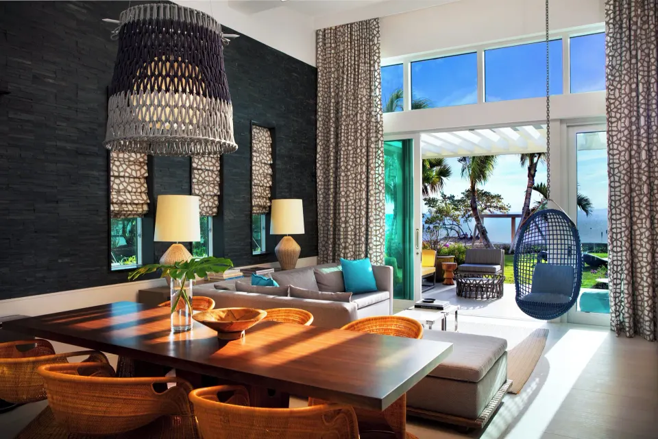 Dining table and lounge with hanging chair beside sliding doors to garden and ocean at Kimpton Seafire Resort + Spa
