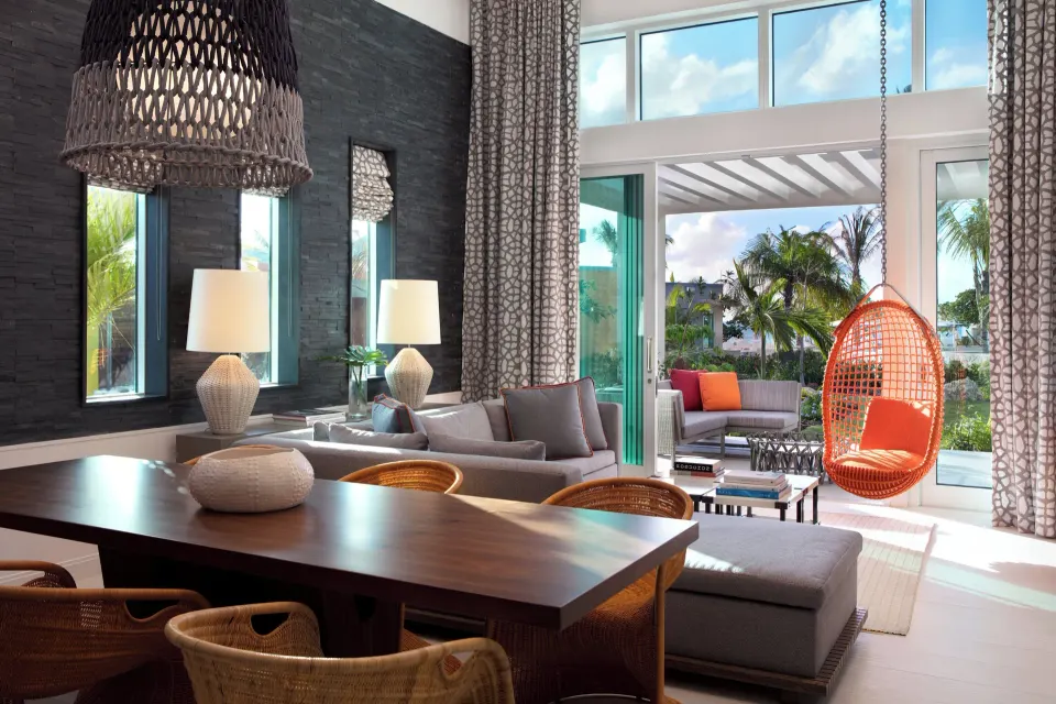 Dining table with woven chairs and sofa area leading to outdoor lounge and palms at Kimpton Seafire Resort + Spa