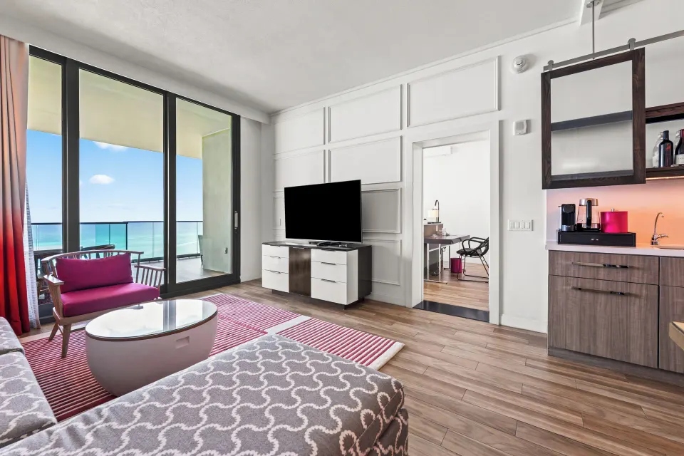 Living room view with TV, minibar and balcony showing ocean in an Oceanfront One-Bedroom Suite at Kimpton Seafire Resort + Sp