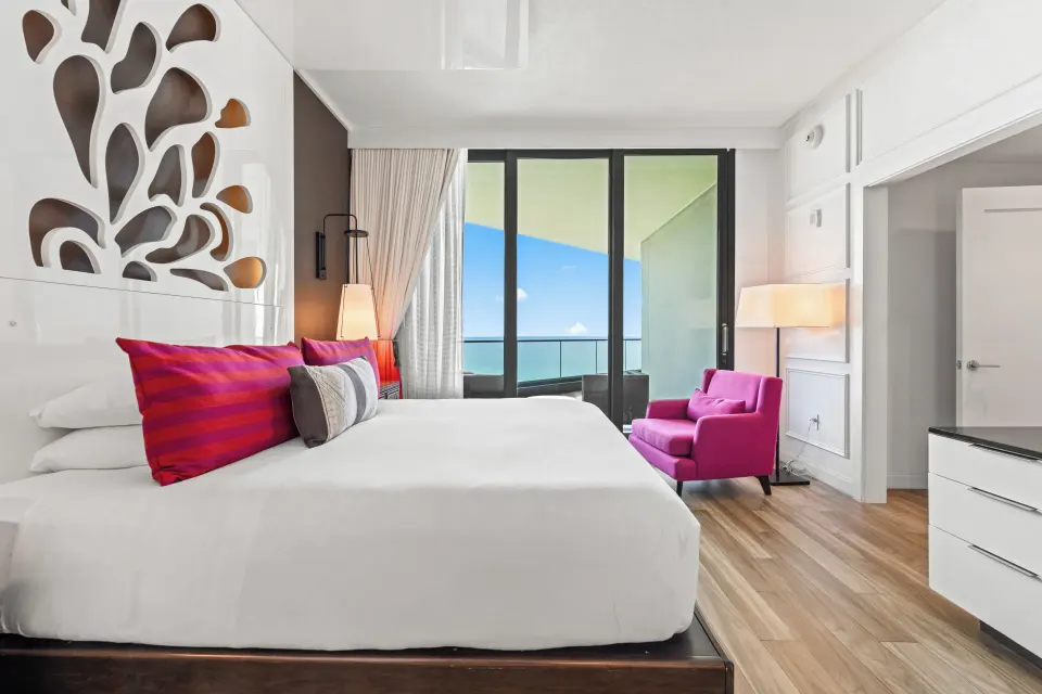 King bed and pink armchair near balcony with ocean view in a Premium Ocean View One-Bedroom Family Suite at Kimpton Seafire R