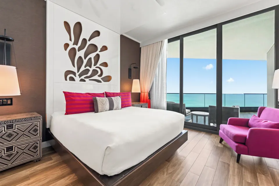 King bed and pink armchair beside ocean-view balcony in a Premium Ocean View One-Bedroom Family Suite at Kimpton Seafire Reso