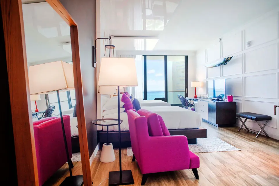 Seating area and mirror view toward beds and balcony in a Premium Ocean View Queen Room at Kimpton Seafire Resort + Spa