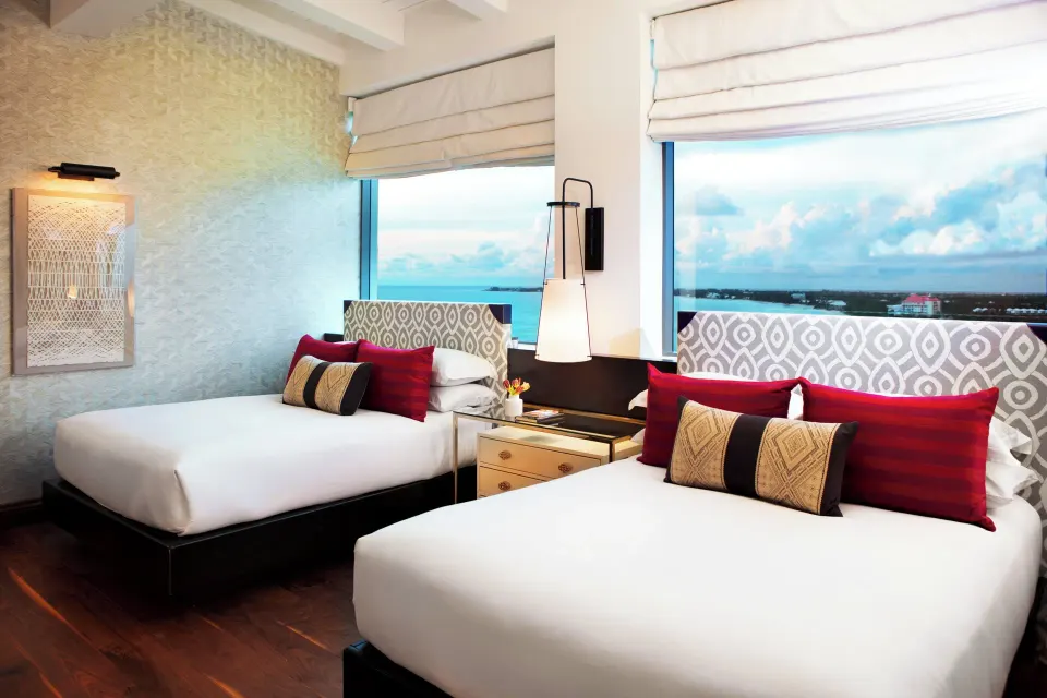 Second bedroom with two beds and decorative red pillows in the Presidential Oceanfront Two-Bedroom Suite at Kimpton Seafire R