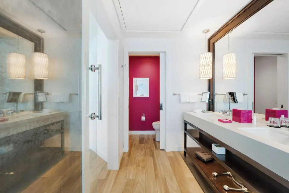Bathroom vanity, glass shower and separate pink-walled toilet room in Yacht Club View King Room at Kimpton Seafire Resort + S