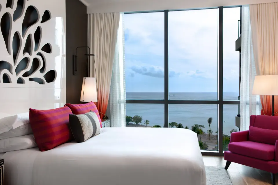 Bright Yacht Club View King room with king bed and pink accent chair at Kimpton Seafire Resort + Spa