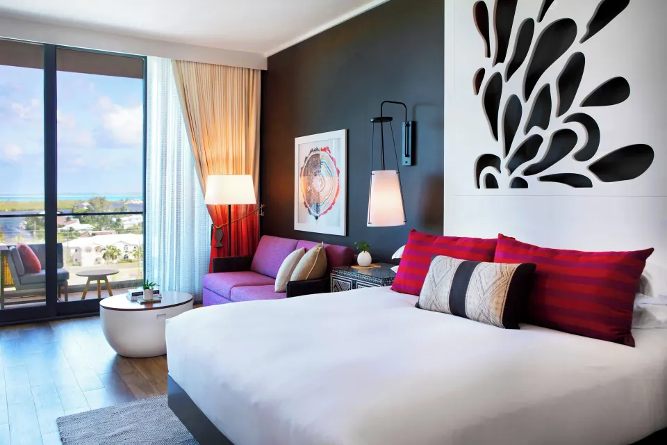 King bed and sofa with balcony doors open to marina view in Yacht Club View King at Kimpton Seafire Resort + Spa