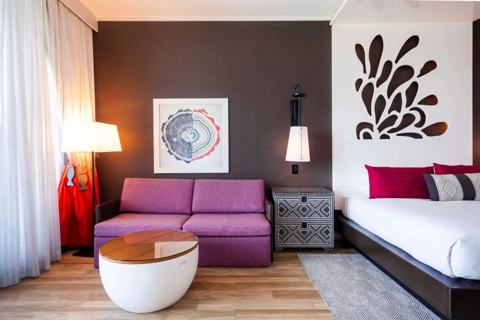 Purple sofa and coffee table beside king bed in a Yacht Club View King Room at Kimpton Seafire Resort + Spa