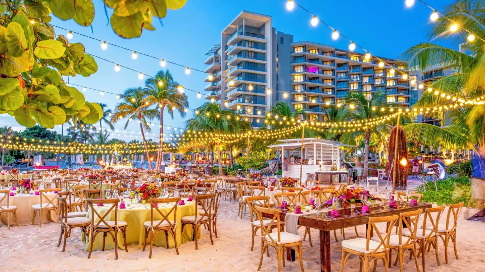 Twilight beach event with string lights and tables set for a reception at Kimpton Seafire Resort + Spa