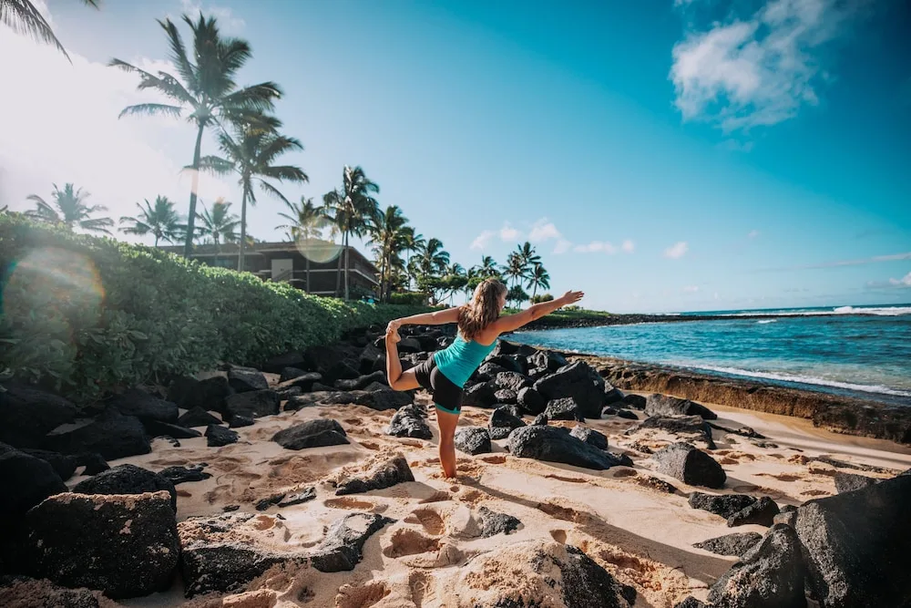Person practicing yoga on the sandy rocky beach at Ko'a Kea Resort on Po'ipu Beach.