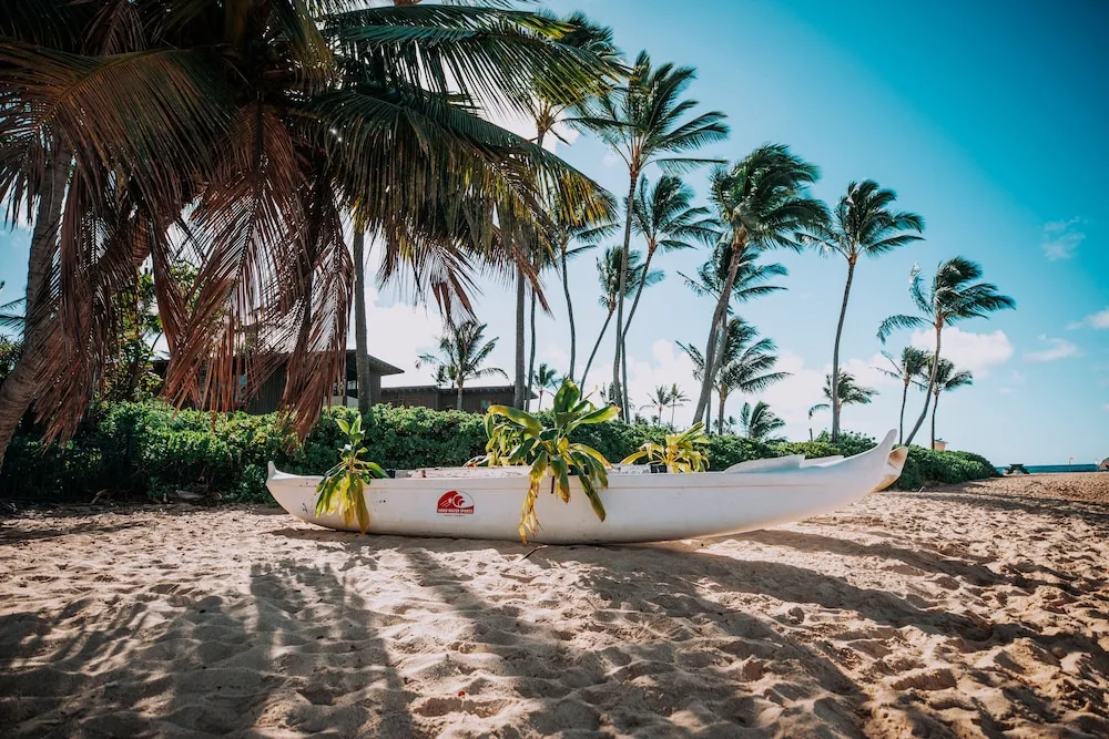 A white outrigger canoe rests on the sand near palms at Ko'a Kea Resort on Po'ipu Beach.