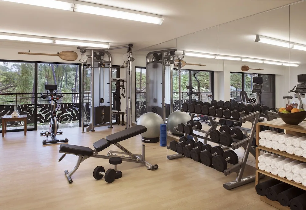 Fitness room with weights, cardio equipment, bench, towels, and mirrors at Ko'a Kea Resort on Po'ipu Beach.