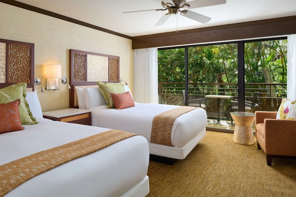 Guest room with two beds and balcony facing tropical greenery at Ko'a Kea Resort on Po'ipu Beach.