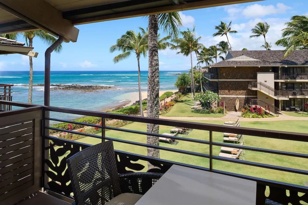 Balcony seating overlooks the ocean, lawns, and palms at Ko'a Kea Resort on Po'ipu Beach.