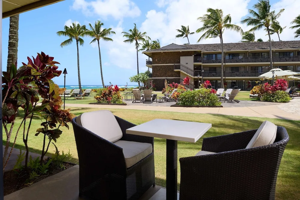 Patio seating overlooks lawns, palms, and the ocean at Ko'a Kea Resort on Po'ipu Beach.