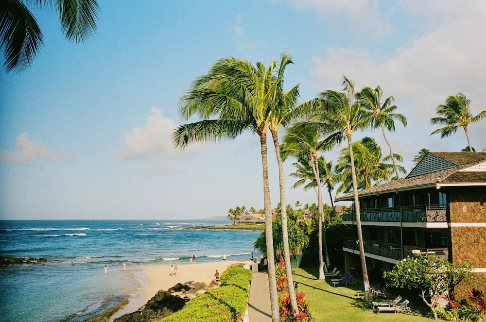 Oceanfront lawn, palms, beach, and resort building at Ko'a Kea Resort on Po'ipu Beach.