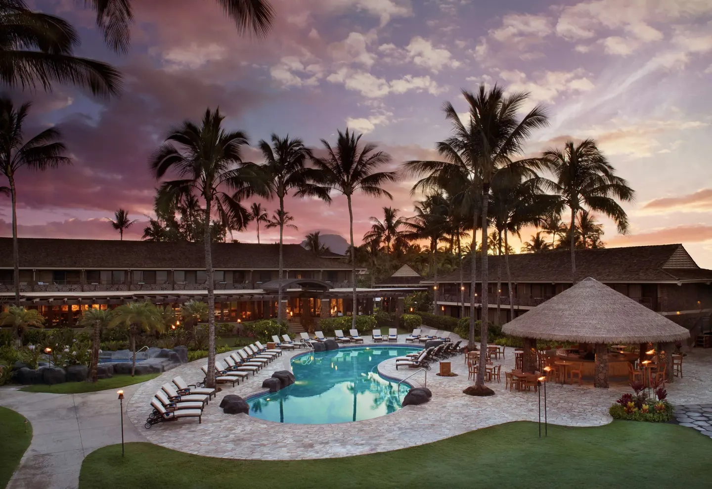 Pool courtyard at Ko'a Kea Resort on Po'ipu Beach at sunset with lounge chairs and a thatched bar.