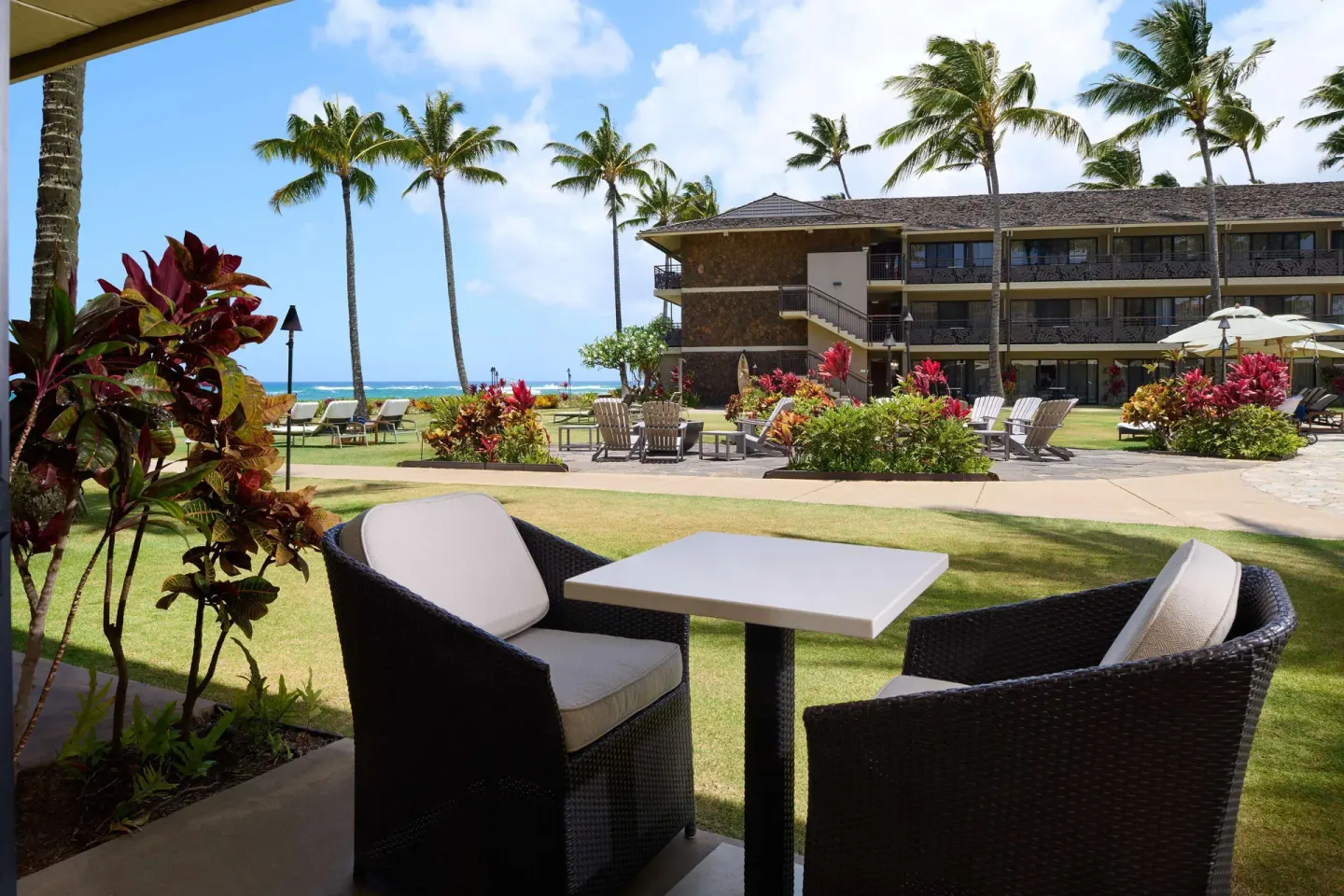 Garden patio seating with lawn, palms, and ocean beyond at Ko'a Kea Resort on Po'ipu Beach.