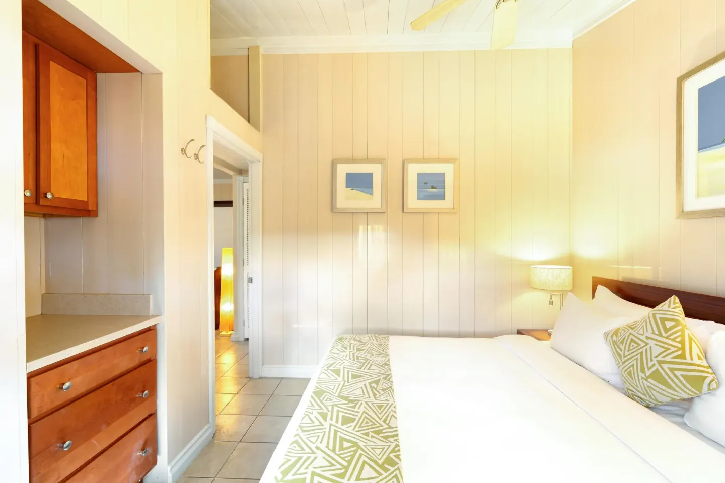 Guest room bed with built-in wood drawers and an open doorway at Kokomo Botanical Resort.