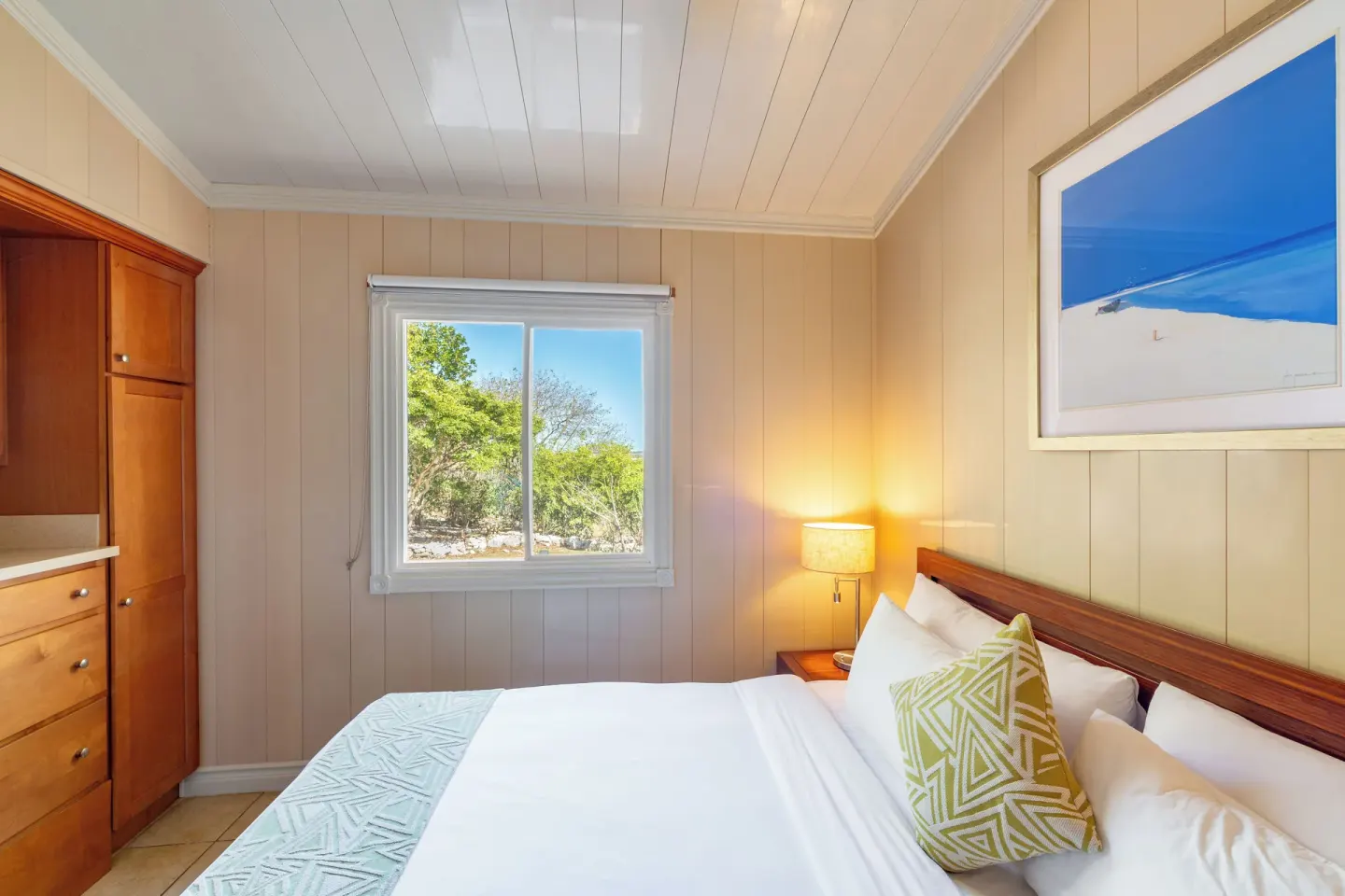 Guest room bed beside a window with greenery outside at Kokomo Botanical Resort.