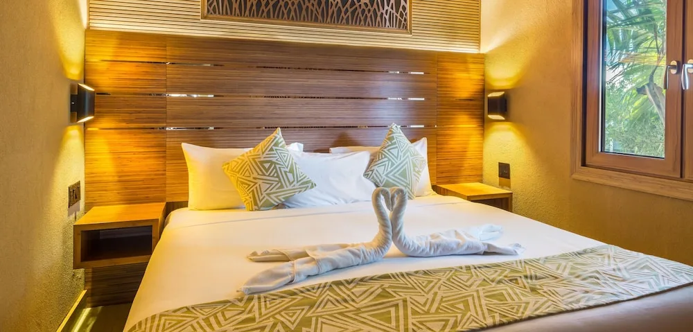 King bed with towel swans in a warm wood guest room at Kokomo Botanical Resort.