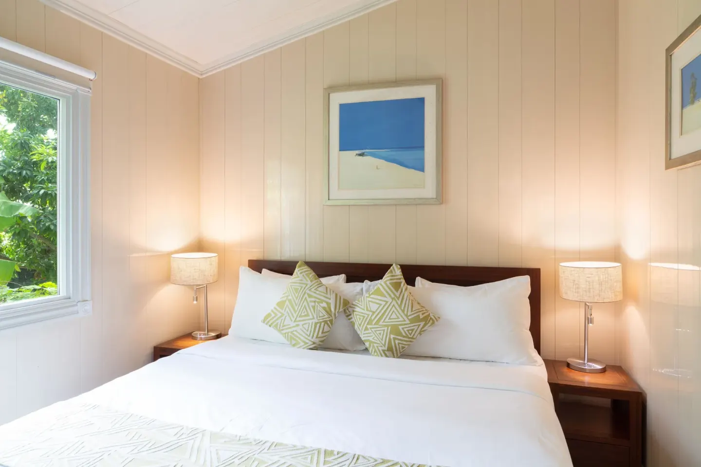 Bright guest room with a large bed, lamps, and beach artwork at Kokomo Botanical Resort.