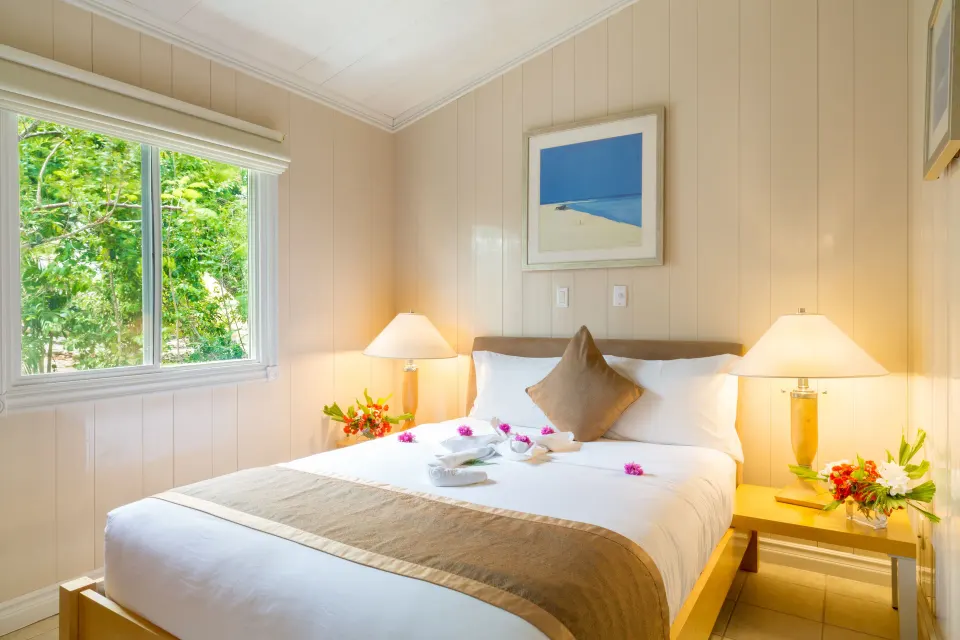 Guest room with a queen bed, lamps, and garden window at Kokomo Botanical Resort.