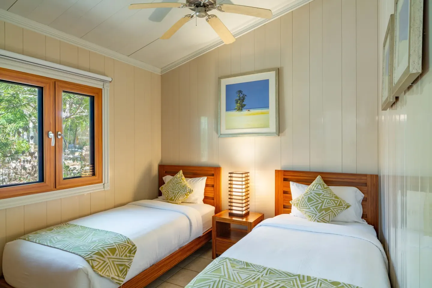 Twin bedroom with two wood beds and a ceiling fan at Kokomo Botanical Resort.