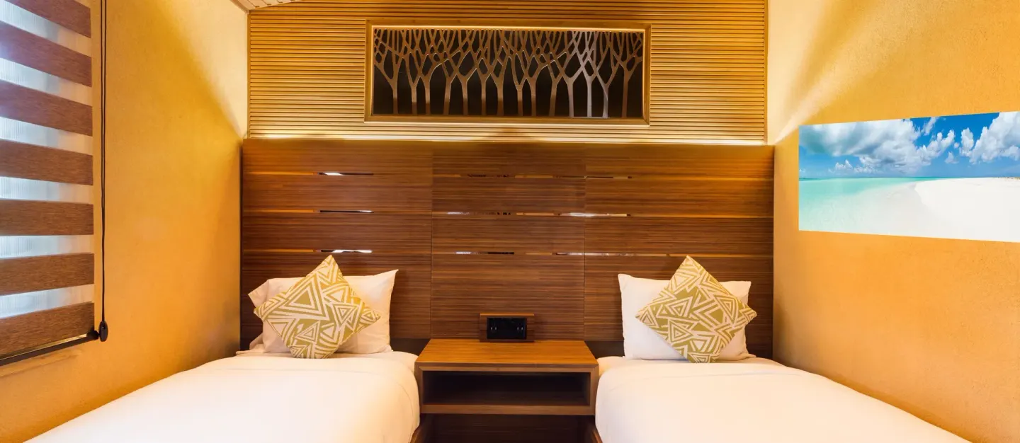 Twin beds with a shared nightstand and beach artwork at Kokomo Botanical Resort.