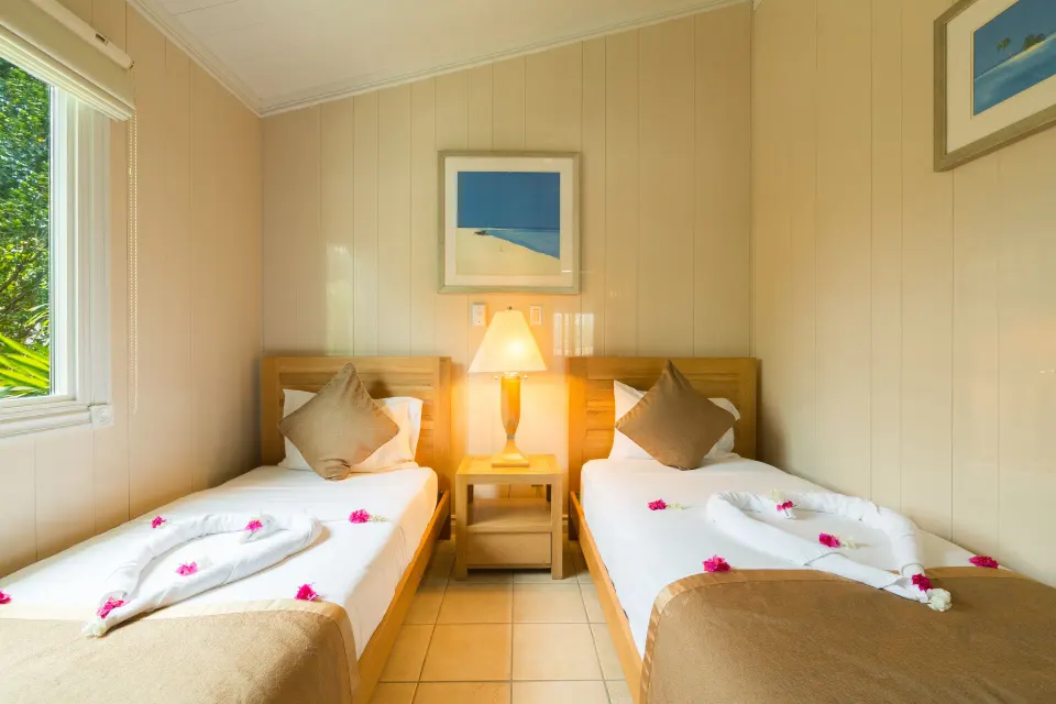 Twin-bed guest room with bedside lamp and window at Kokomo Botanical Resort.