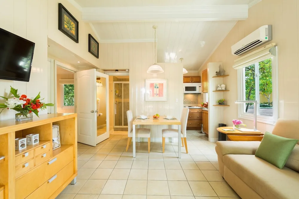 Light-filled suite with sofa, dining table, kitchenette, and bathroom door at Kokomo Botanical Resort.