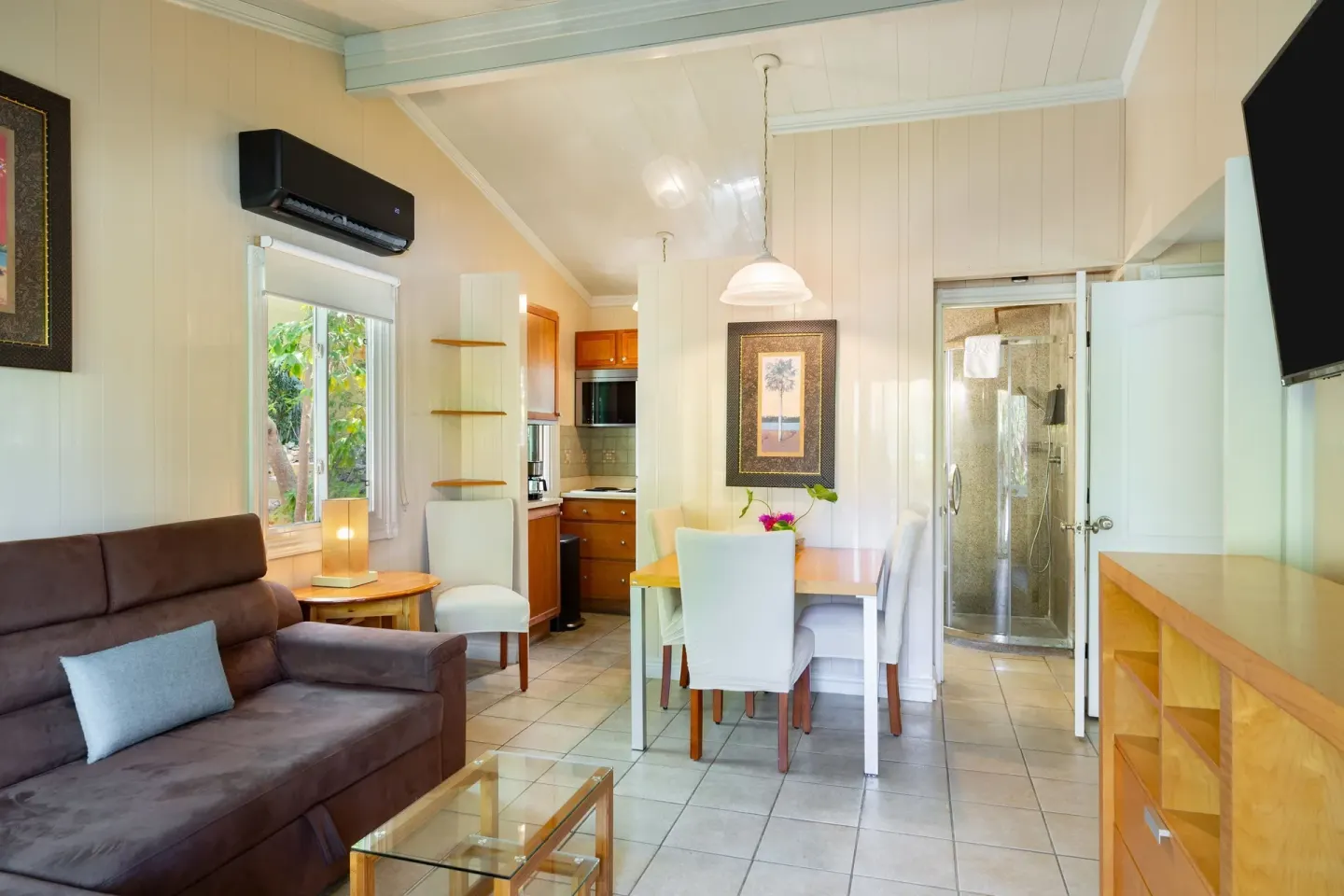 Suite living area with brown sofa, dining table, kitchenette, and shower at Kokomo Botanical Resort.