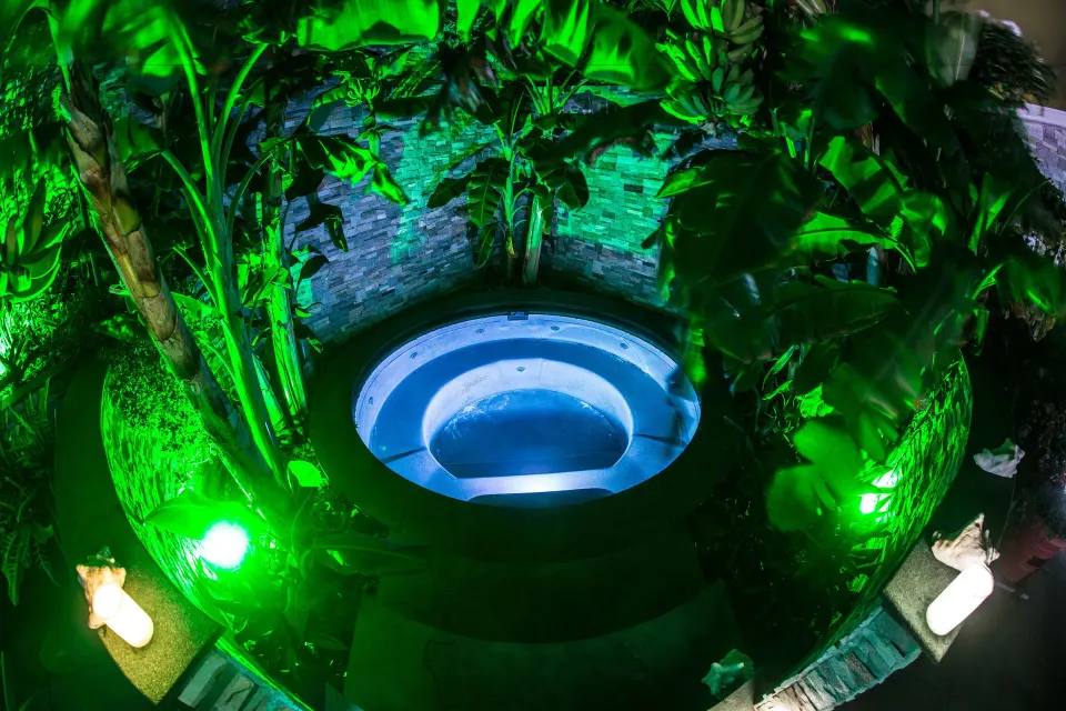 Round spa pool lit in green among tropical plants at Kokomo Botanical Resort.