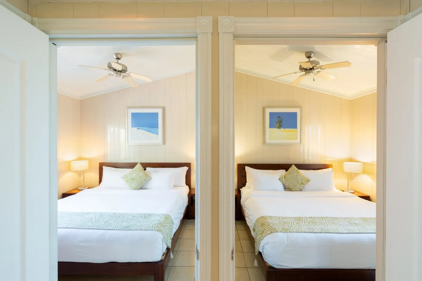 Two adjacent bedrooms with white beds and ceiling fans at Kokomo Botanical Resort.