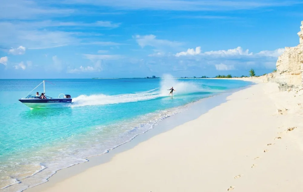 A wakeboarder follows a motorboat along a white-sand beach near Kokomo Botanical Resort.