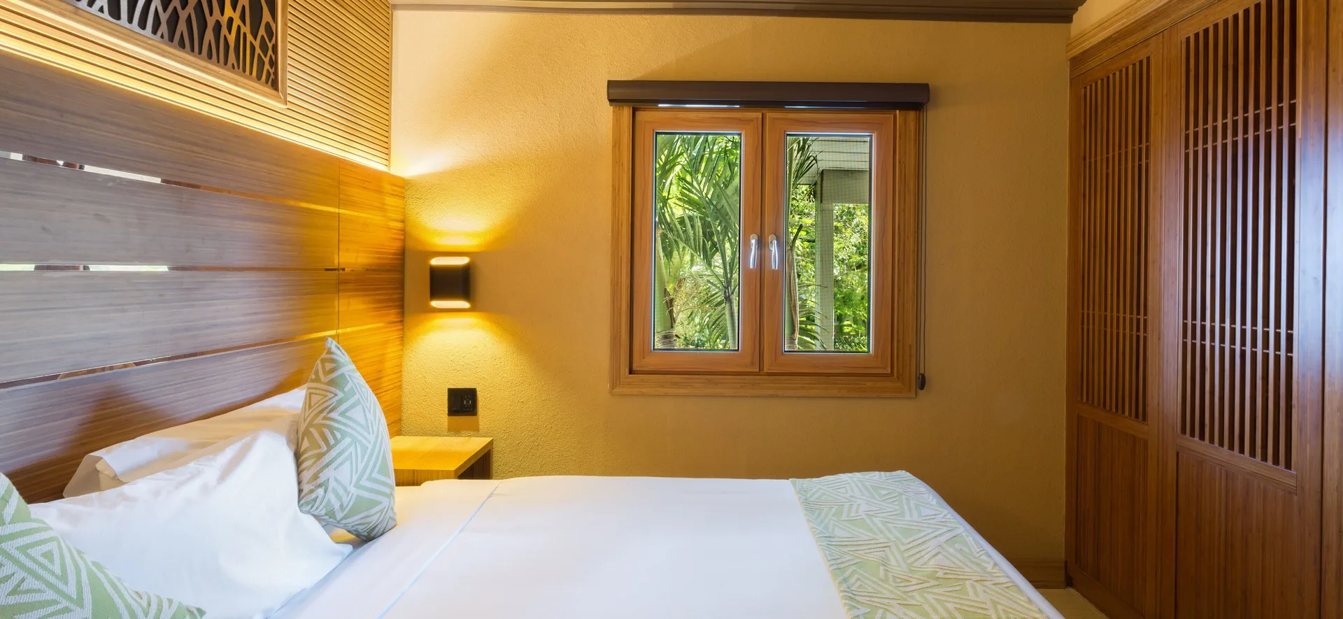Superior Cottage bedroom with bed, garden window, and wood wardrobe at Kokomo Botanical Resort.