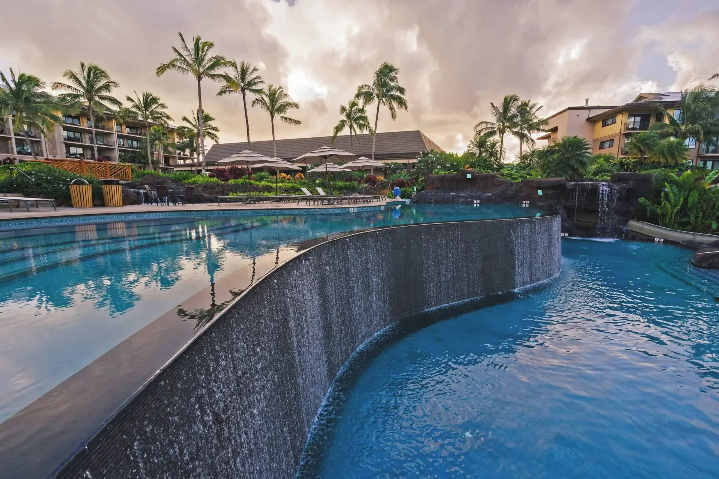 Curved pool wall with water feature and palm-lined deck at Koloa Landing Resort at Poipu.