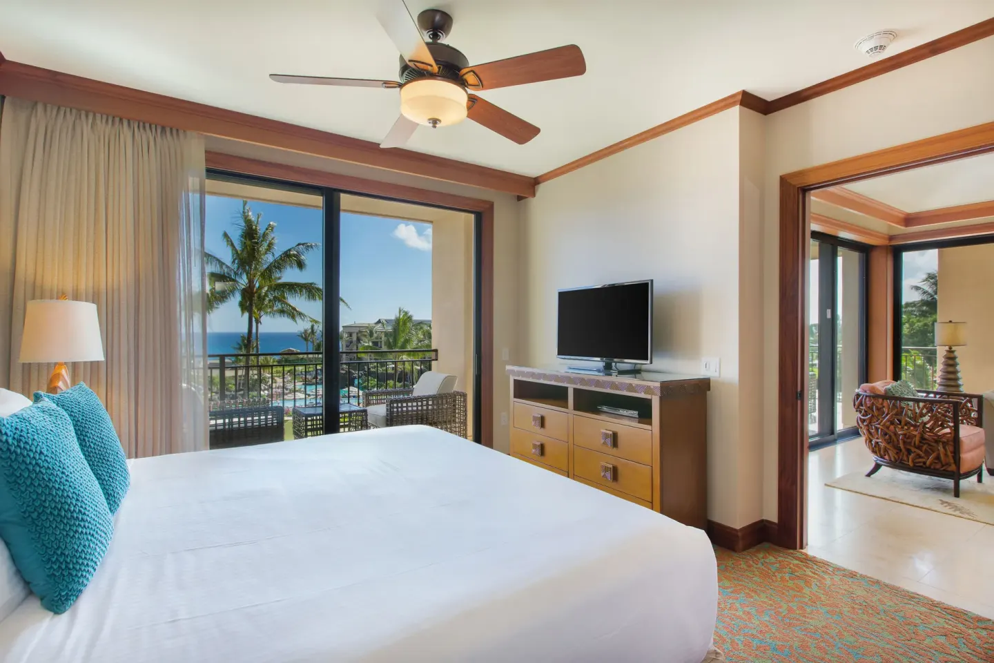 Guest bedroom with balcony, TV, and adjoining sitting area at Koloa Landing Resort at Poipu.