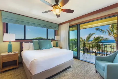 King bedroom with blue accents and ocean balcony at Koloa Landing Resort at Poipu.