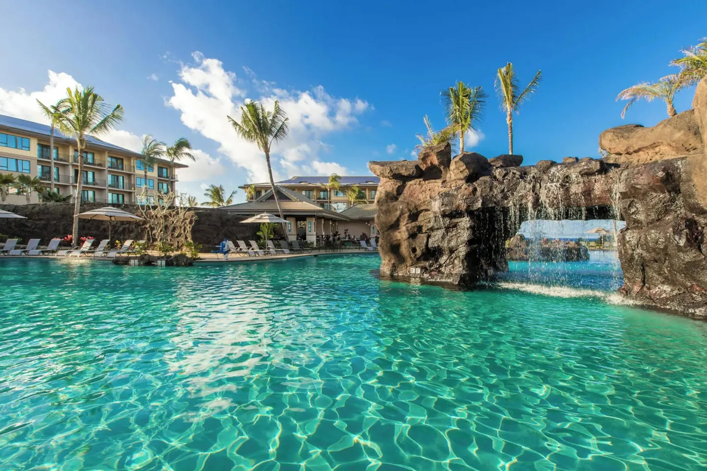 Large pool with a lava-rock waterfall and guest buildings at Koloa Landing Resort at Poipu.