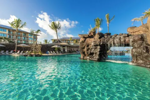 Large pool with a lava-rock waterfall and guest buildings at Koloa Landing Resort at Poipu.