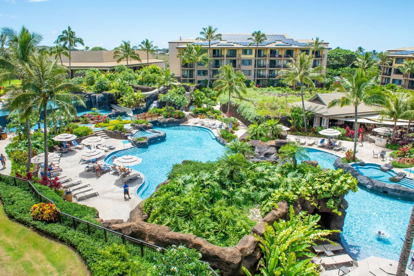 Daytime view of the resort pool, waterfalls, palms, and buildings at Koloa Landing Resort at Poipu.