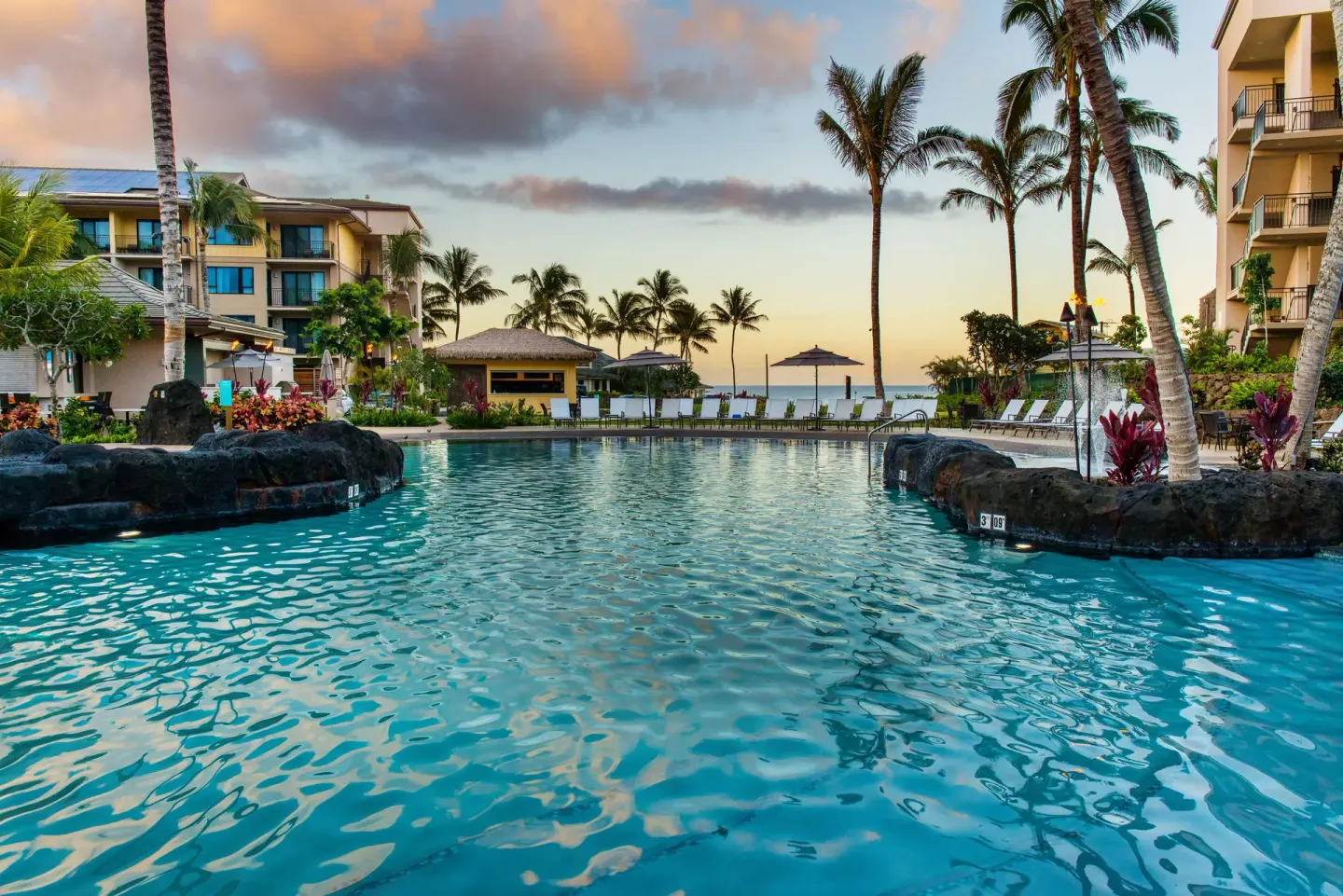 Resort pool with palms, lounge chairs, and ocean beyond at Koloa Landing Resort at Poipu.