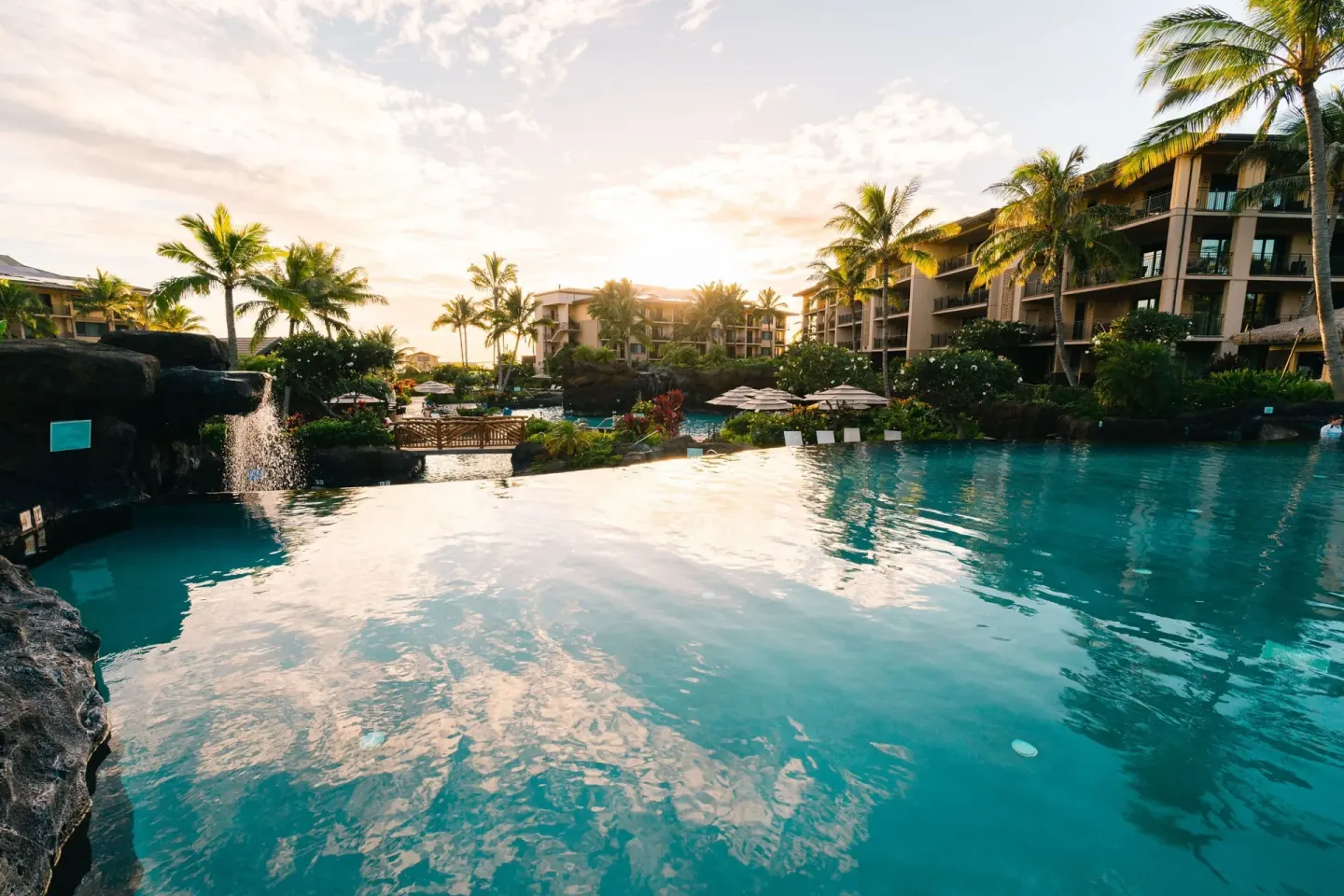 Sunset over the resort pool with palms, waterfall, and guest buildings at Koloa Landing Resort at Poipu.